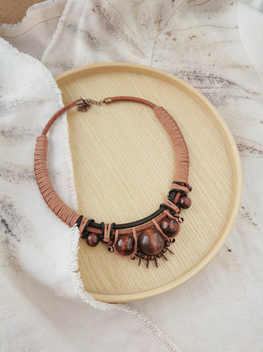 Brown boho beaded necklace on a wooden tray with a textured fabric backgroun