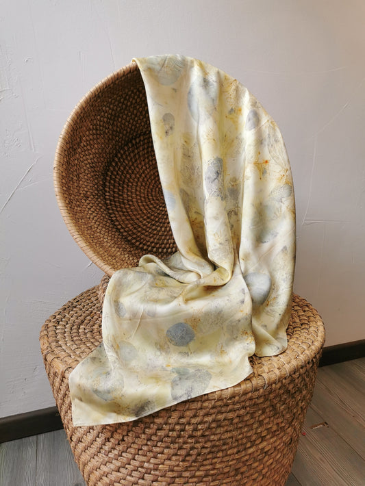 Woven chair with a eco-printed silk scarf draped over it against a plain wall.