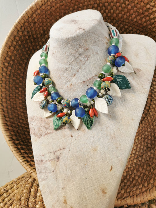 Colorful whimsical floral charm necklace on a stone stand with a woven background