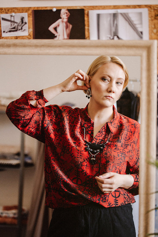 women in red shirt trying an earrings in front of mirror