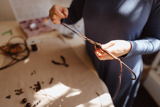 hands holding leather cords and braiding near the table with beads 