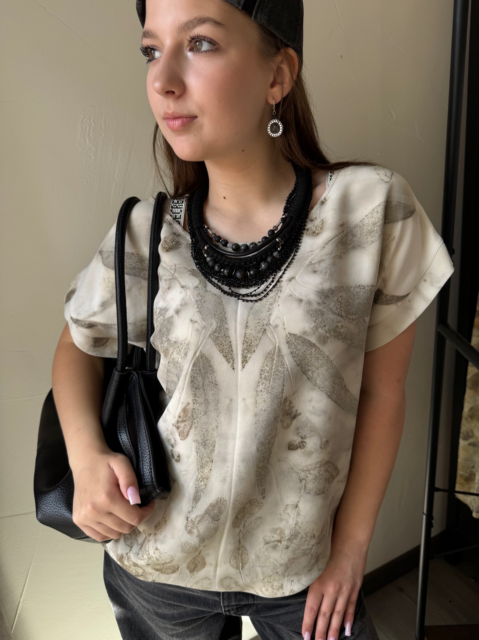 Woman wearing a patterned shirt and holding a black handbag indoors.