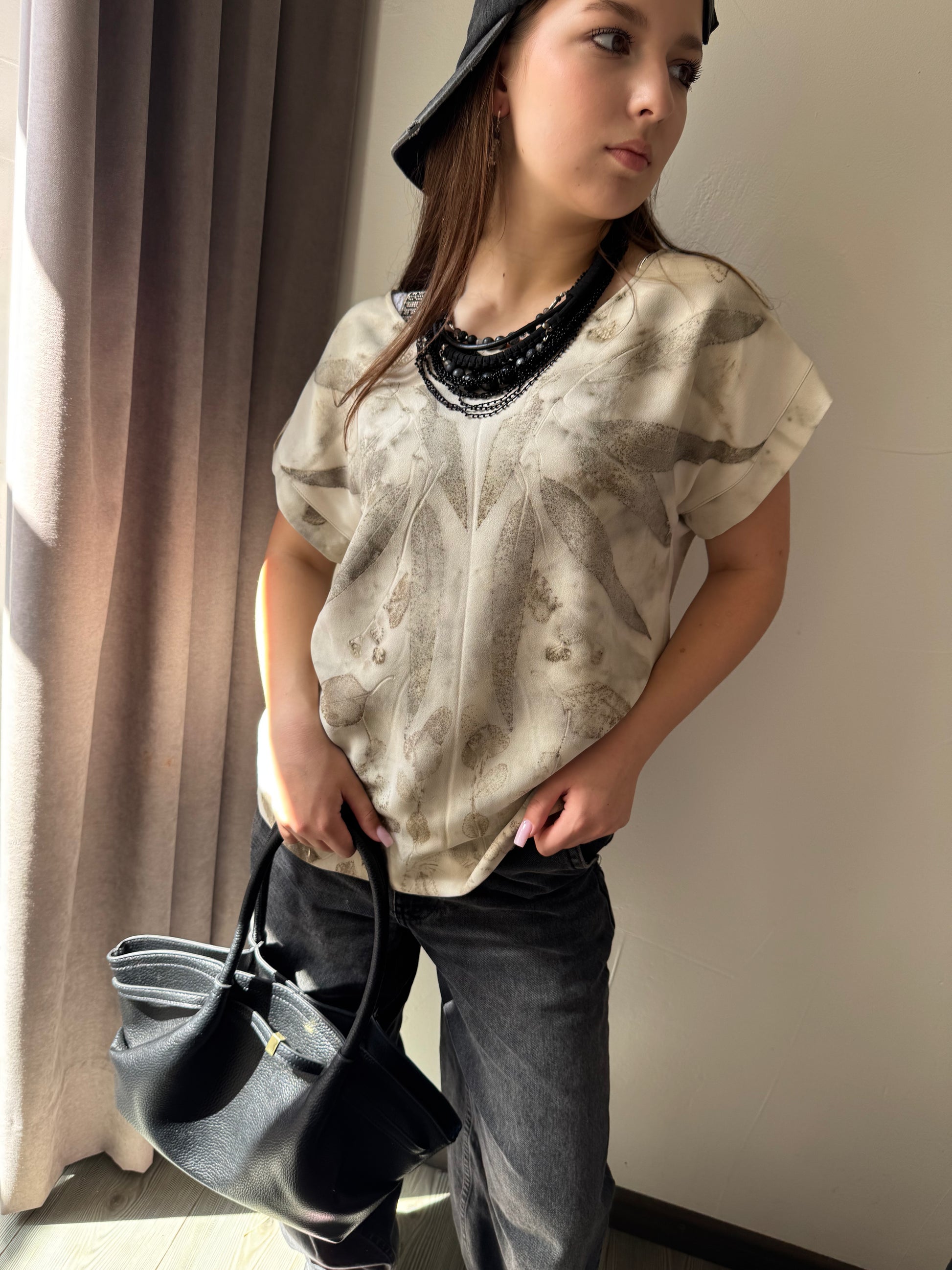 Person wearing a patterned shirt and holding a handbag indoors.