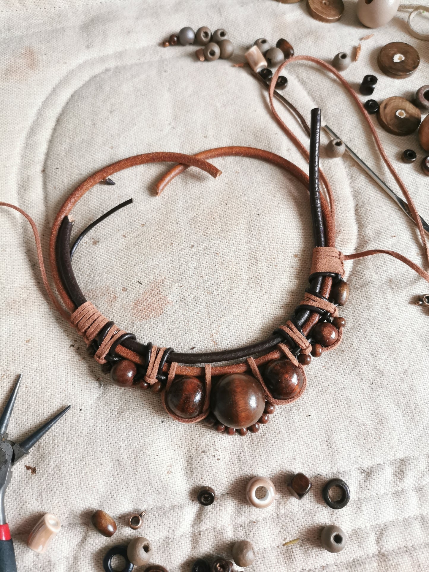 Brown leather and wood bead necklace on a textured surface with tools and beads.