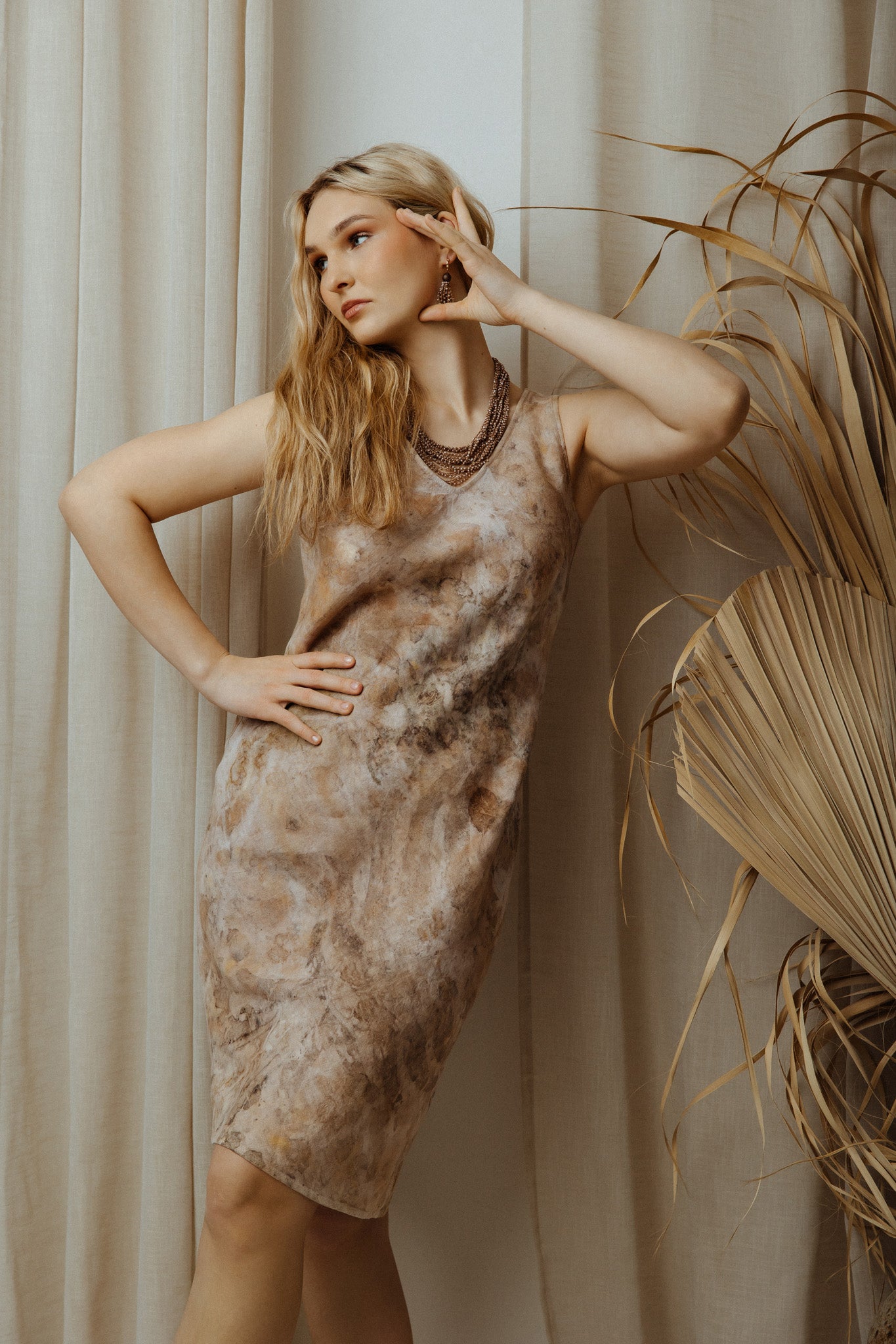 Woman wearing a patterned dress standing against a neutral background with a plant.