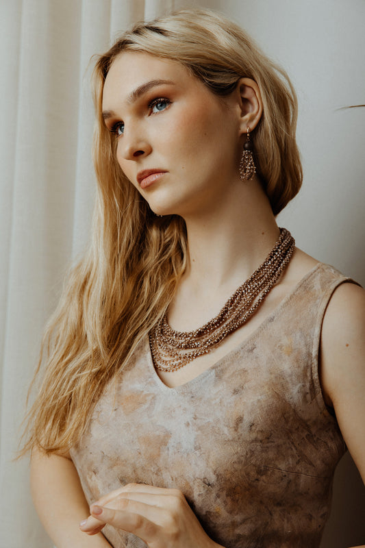 Woman wearing a patterned top and multiple necklaces with a neutral background
