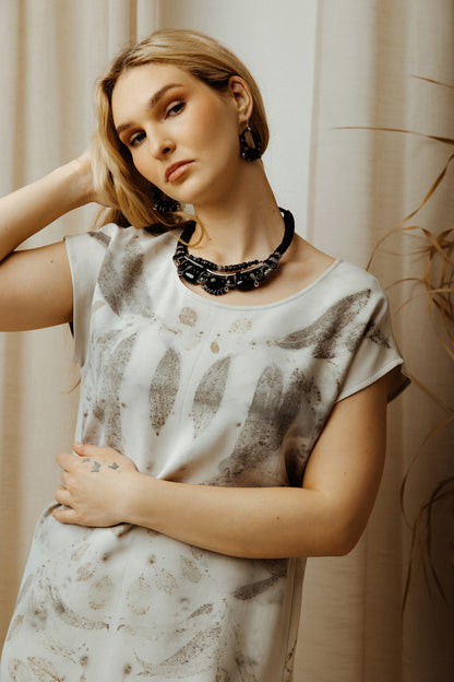Woman wearing a patterned dress and black necklace against a neutral background