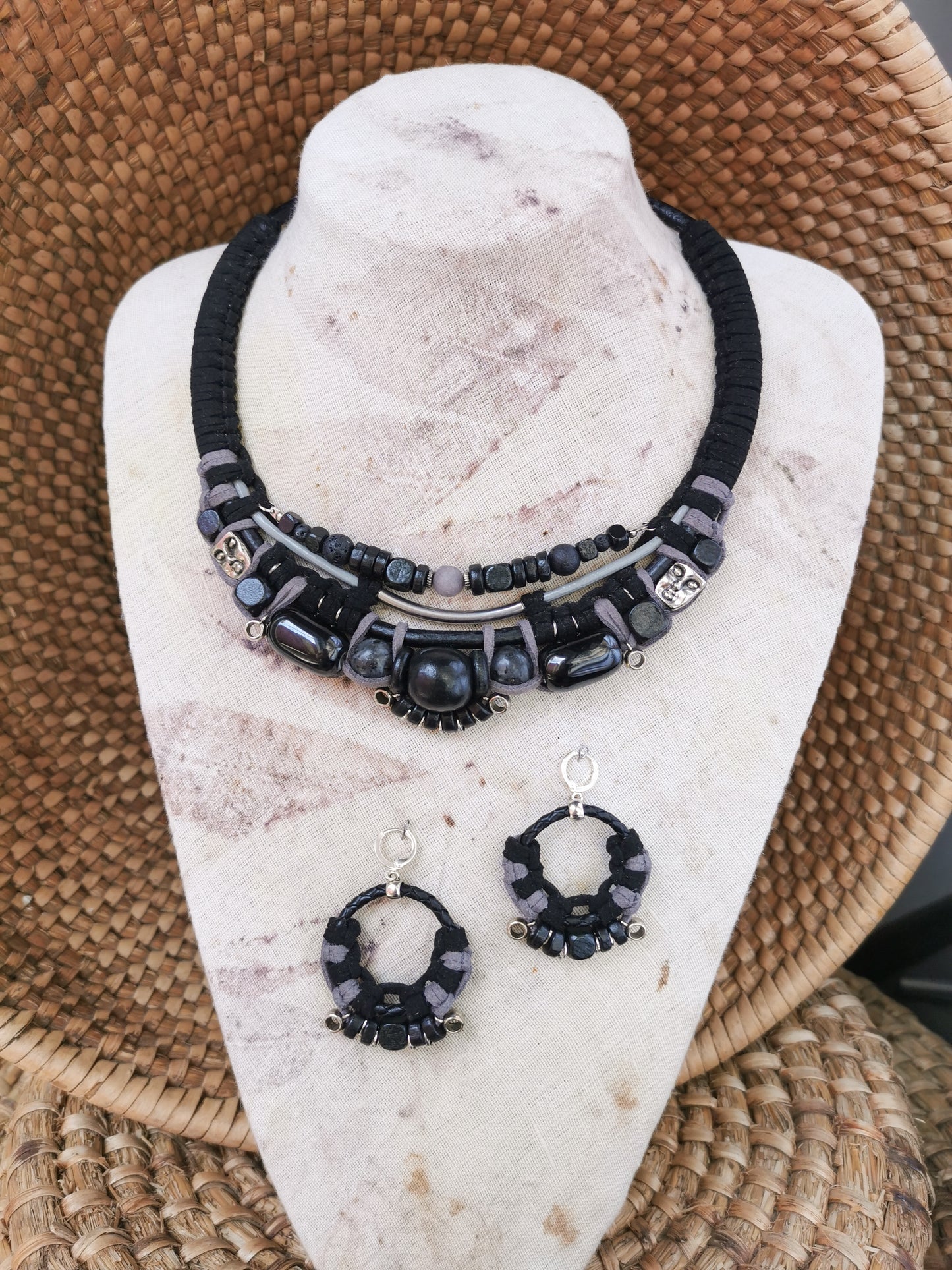 Black beaded necklace and earrings on a white stone stand with a woven surface background