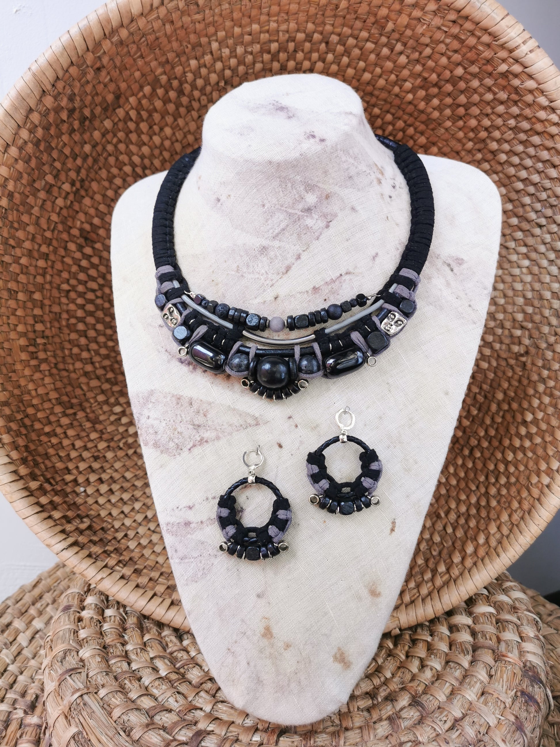 Black beaded necklace and earrings on a white stone stand with a woven basket background
