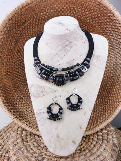 Black beaded necklace and earrings on a white stone stand with a woven basket background