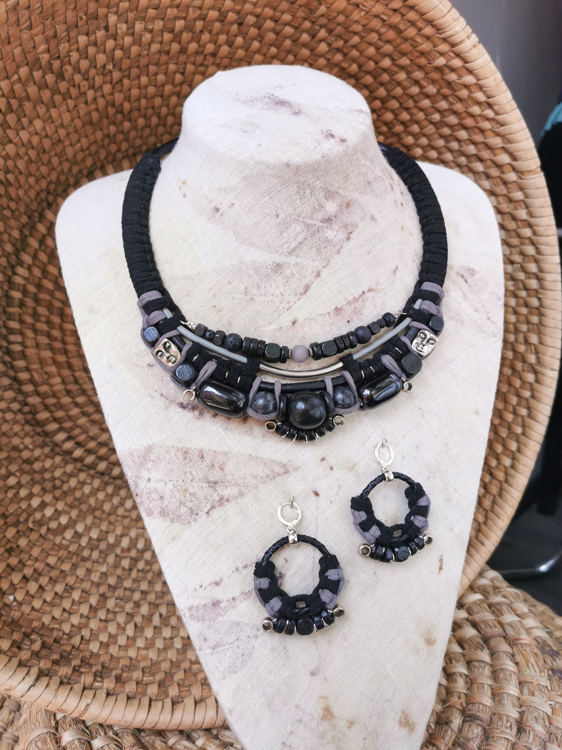 Black beaded necklace and earrings on a white stone stand with a woven surface background.