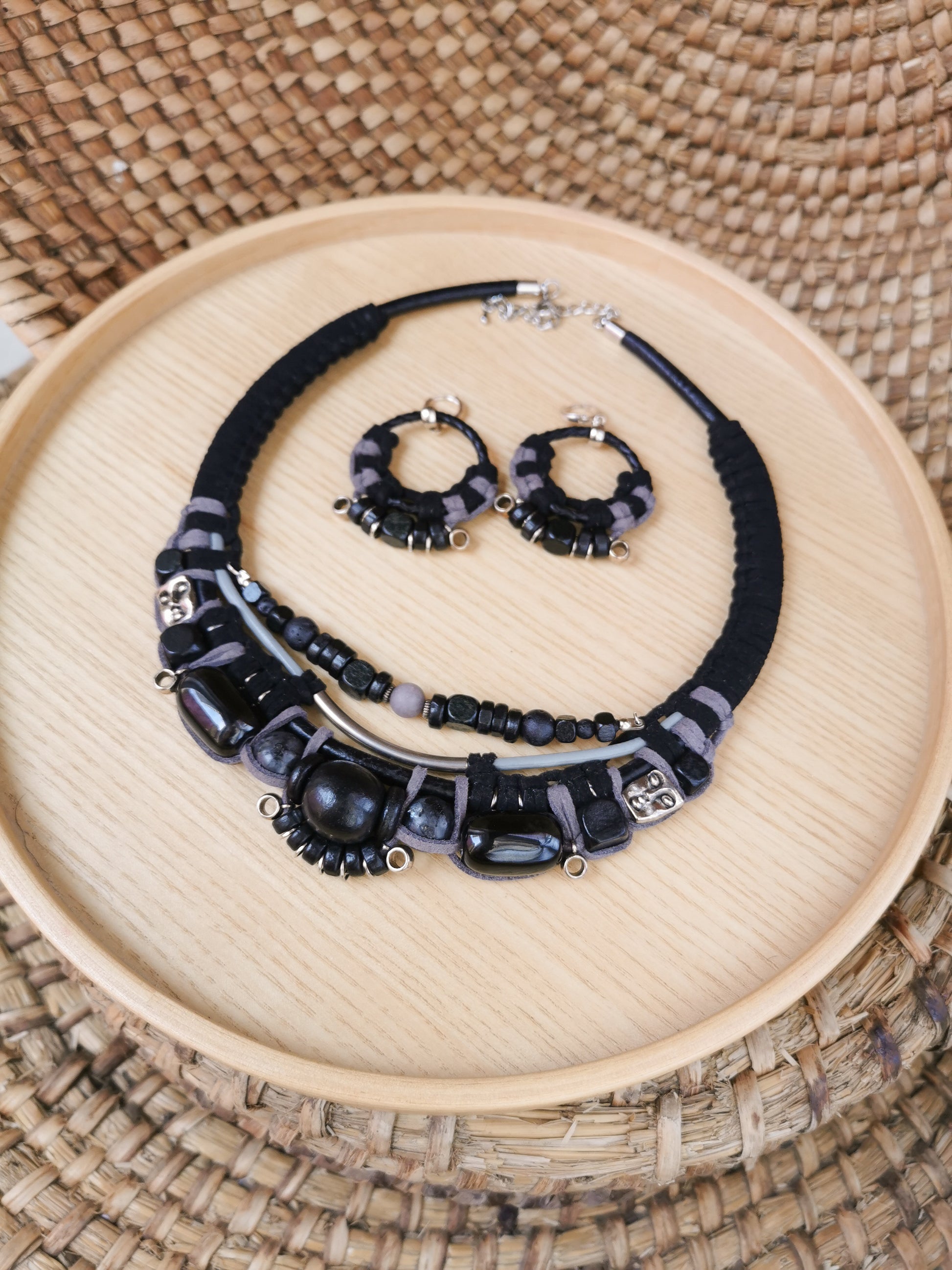 Black beaded necklace and earrings on a wooden tray with a woven background