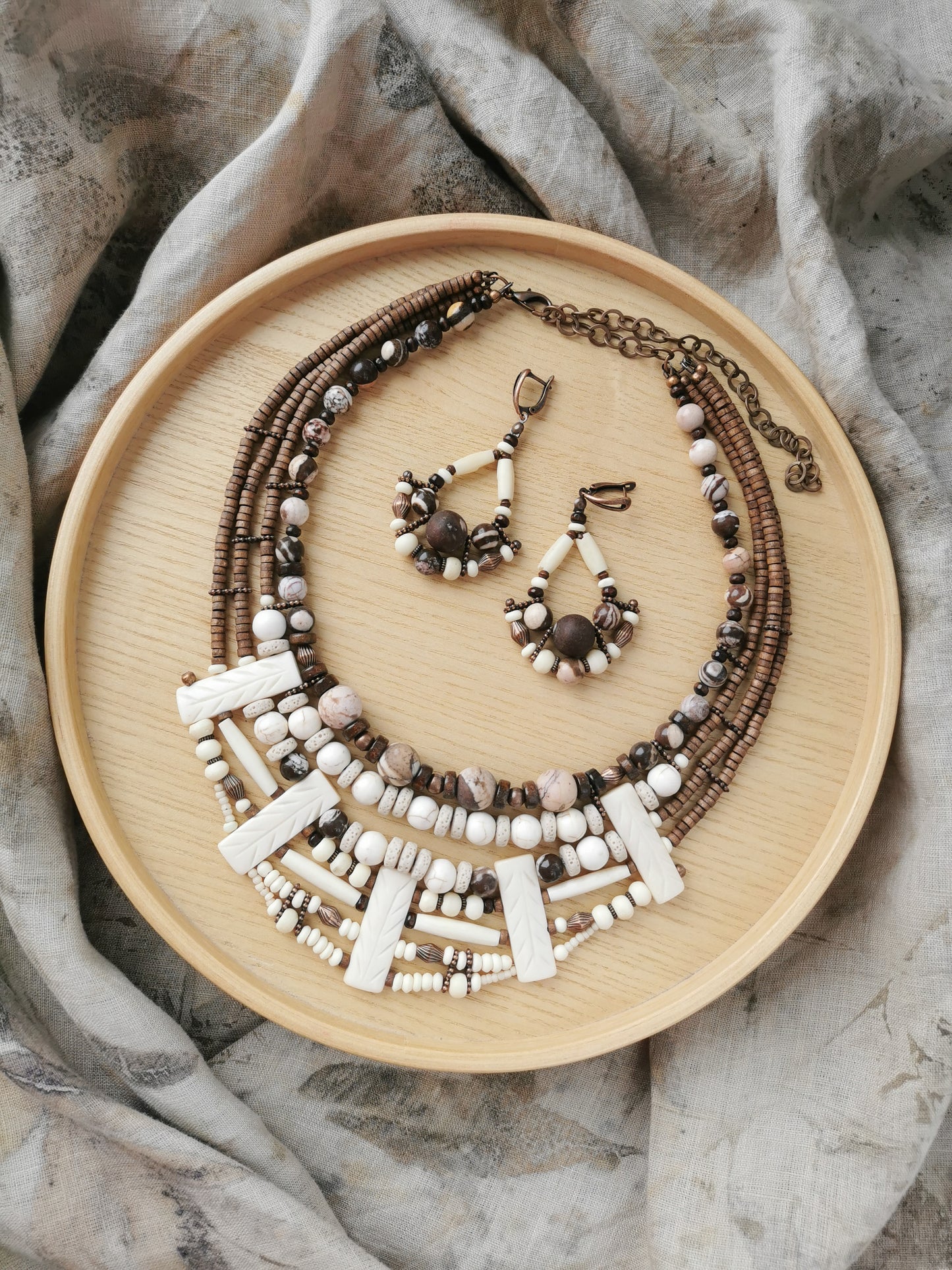 bohemian bead jewelry set including a necklace and earrings on a wooden plate with a neutral background