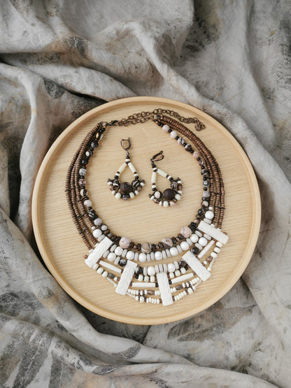 Layering design Necklace and earrings set on a wooden plate with a textured fabric background