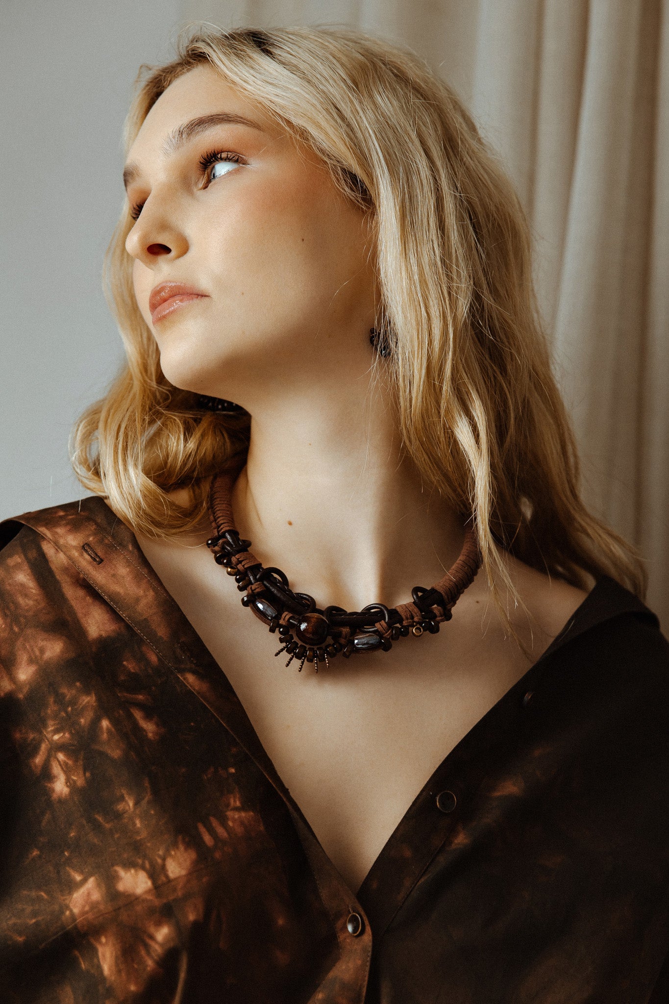 Woman wearing a dark boho rope and bead necklace against a neutral background