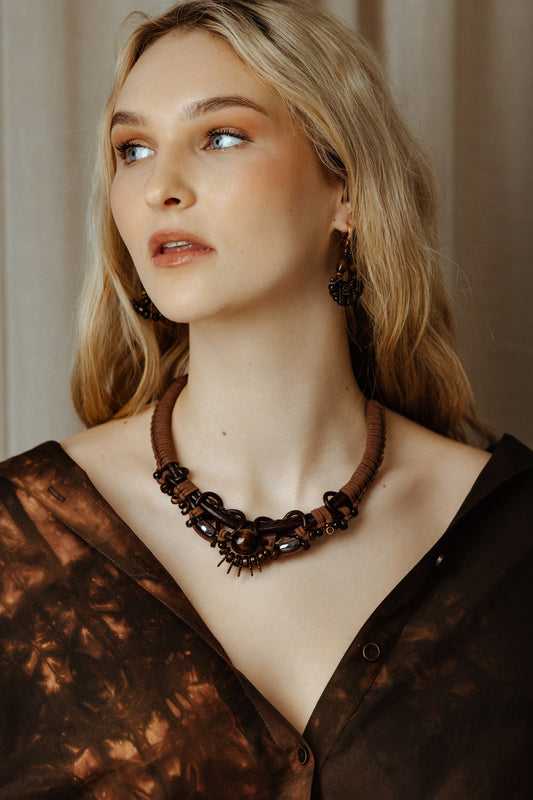 Woman wearing a dark brown necklace and earrings against a neutral background
