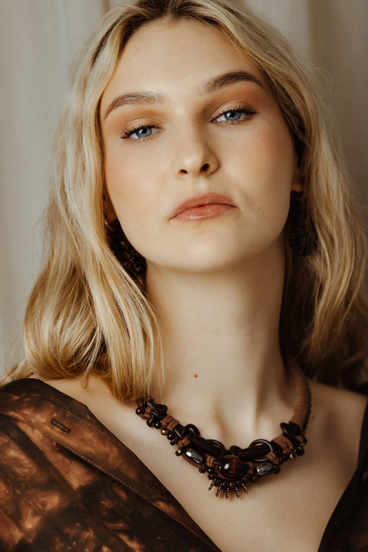 Woman wearing a dark boho rope and bead necklace against a neutral background