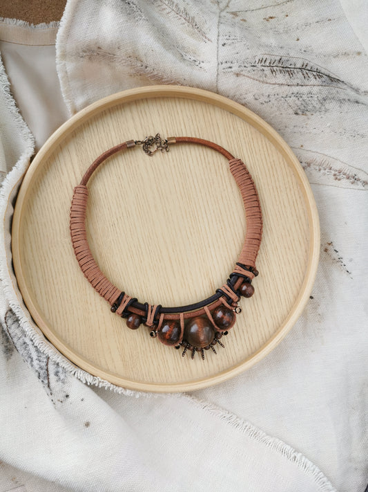 Brown boho beaded necklace on a wooden plate with a textured white fabric background