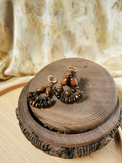 Brown beaded earrings on a wooden stand with a marble background