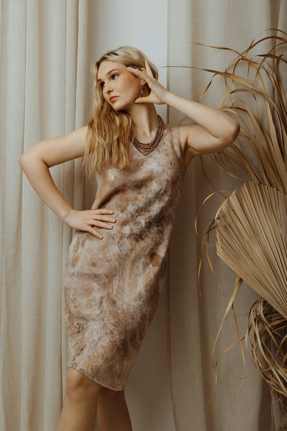 Woman wearing a botanical dye beige linen dress standing against a neutral background with a plant.