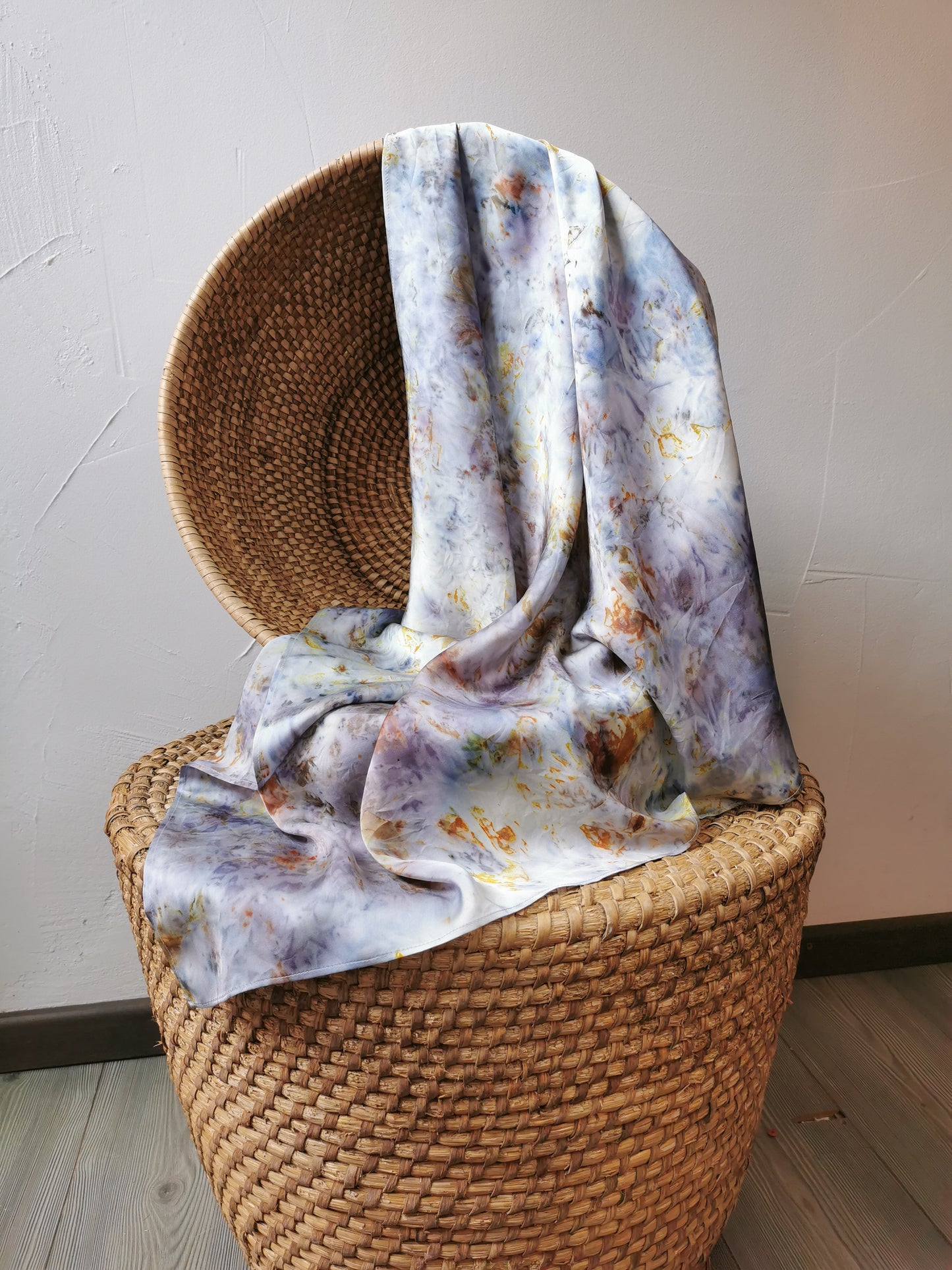 Floral patterned silk scarf draped over a wicker chair against a white wall.