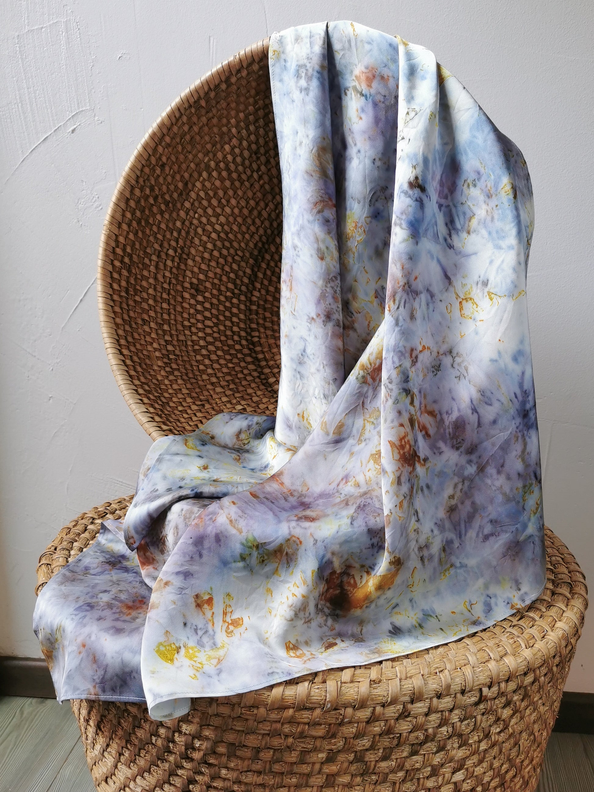 Floral-patterned silk scarf draped over a wicker chair against a neutral wall.