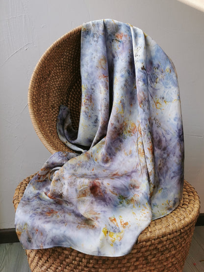 Floral patterned silk scarf draped over a wicker chair against a plain wall.