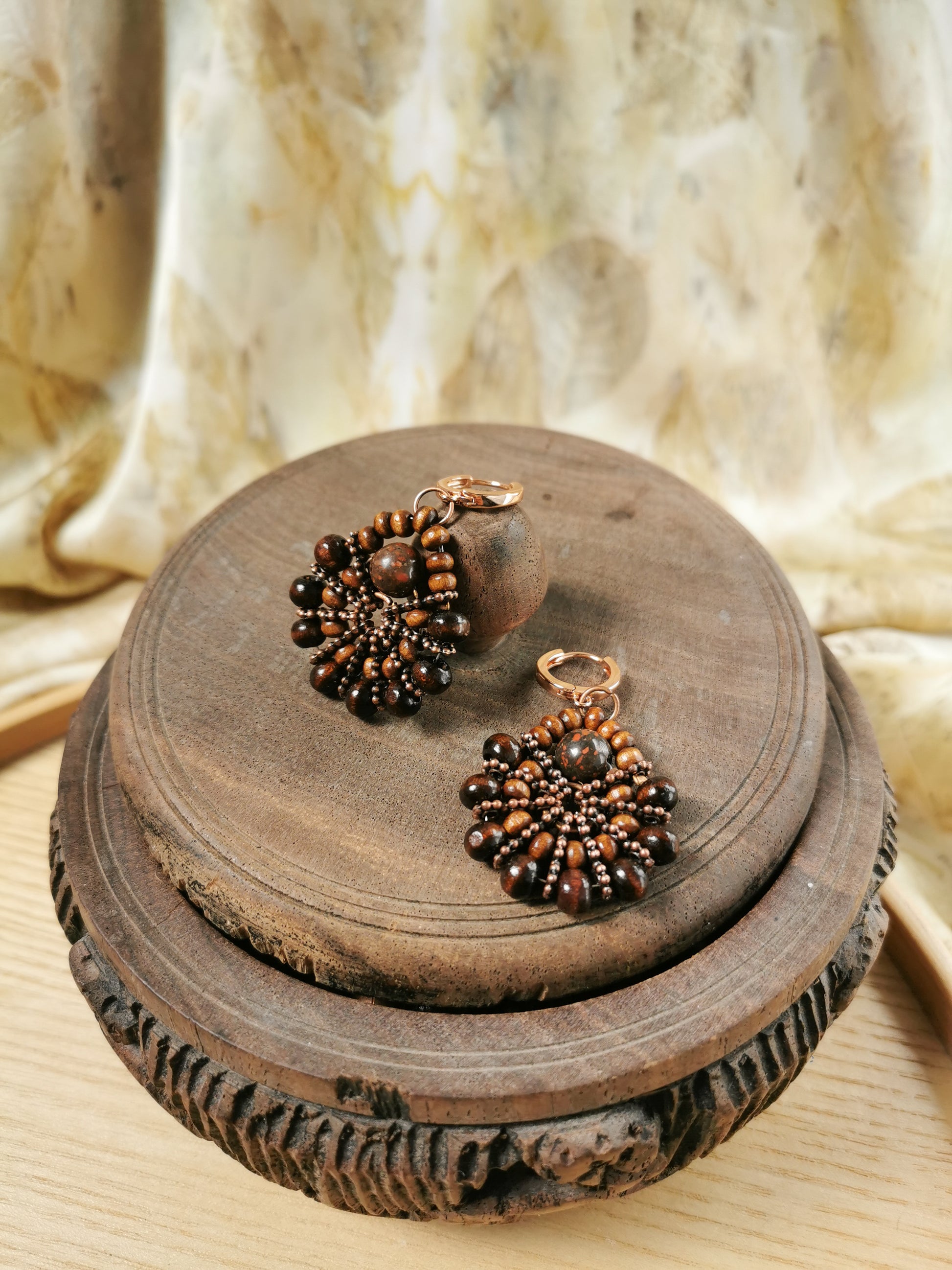 Pair of beaded earrings on a wooden surface with a soft fabric background