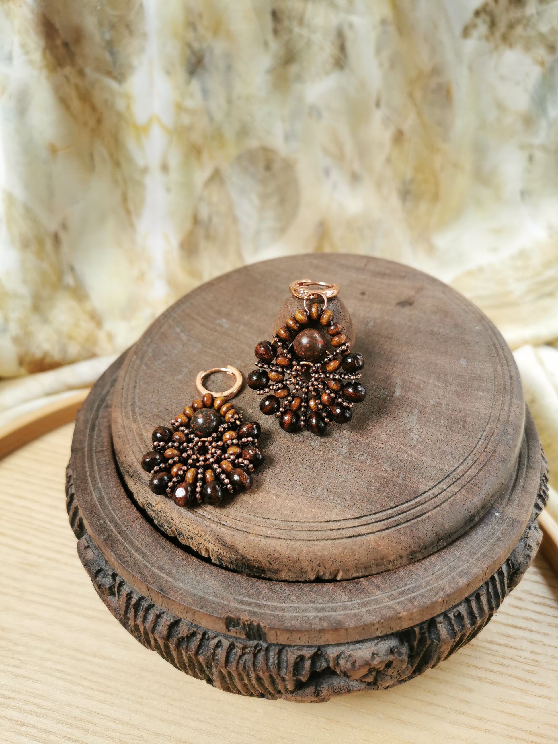 Pair of bronze-colored earrings on a wooden stand with a textured background