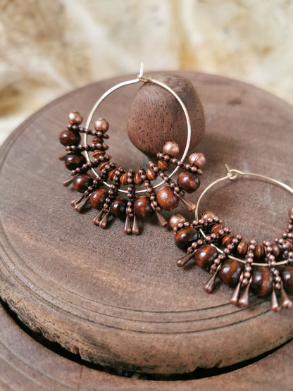 Pair of brown beaded hoop earrings on a wooden surface