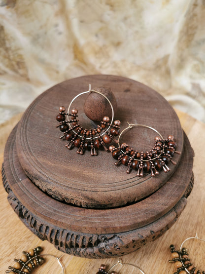 Pair of bronze hoop earrings with beads on a wooden surface