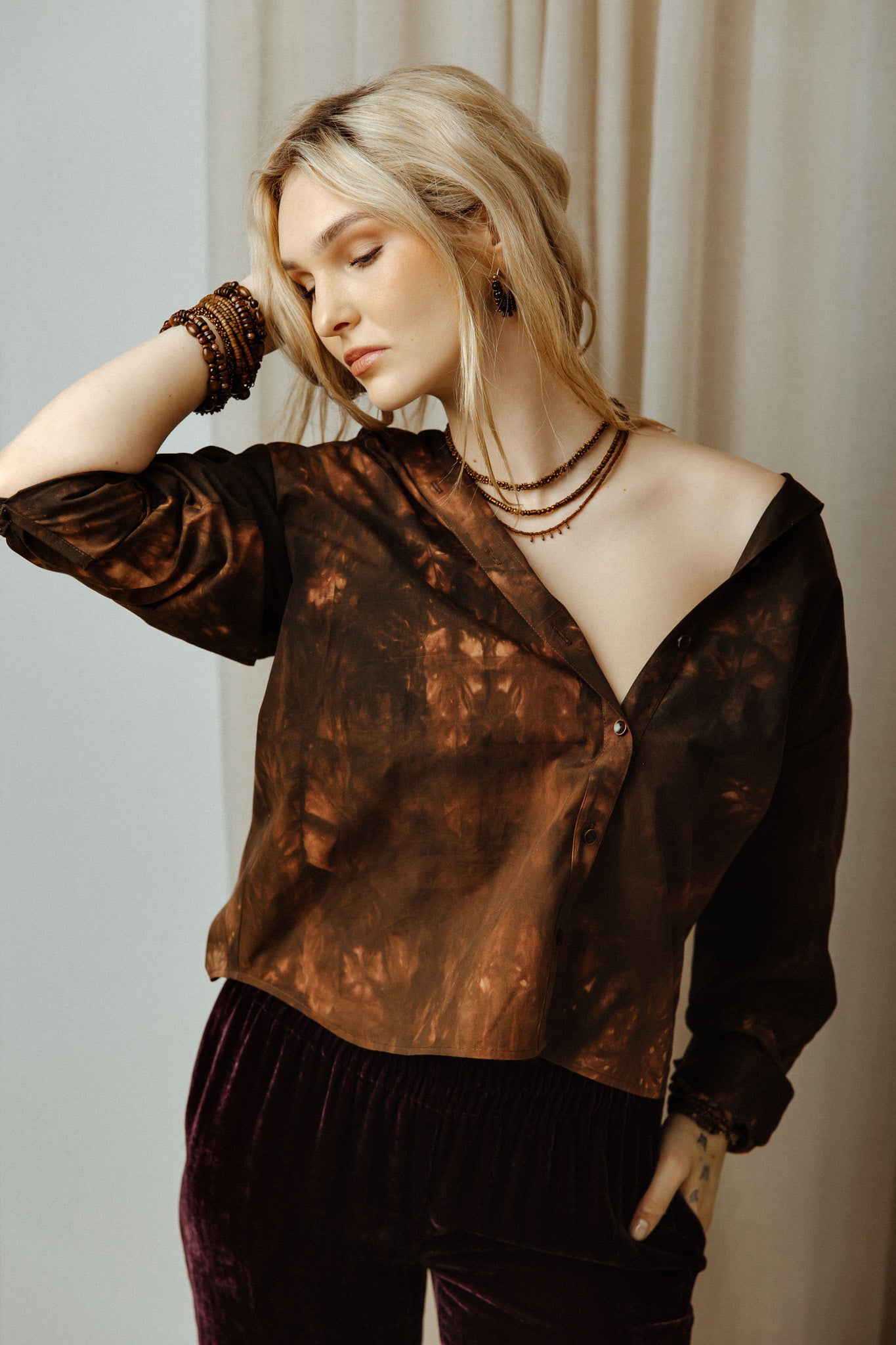 Woman wearing a brown colours tye dye boho shirt and black pants against a neutral background