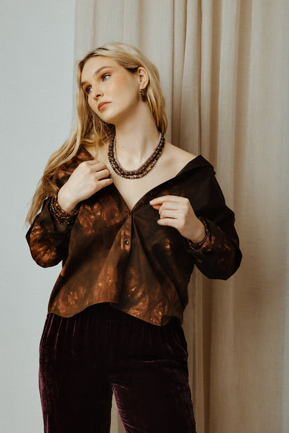 Woman wearing a brown patterned top and dark pants against a neutral background