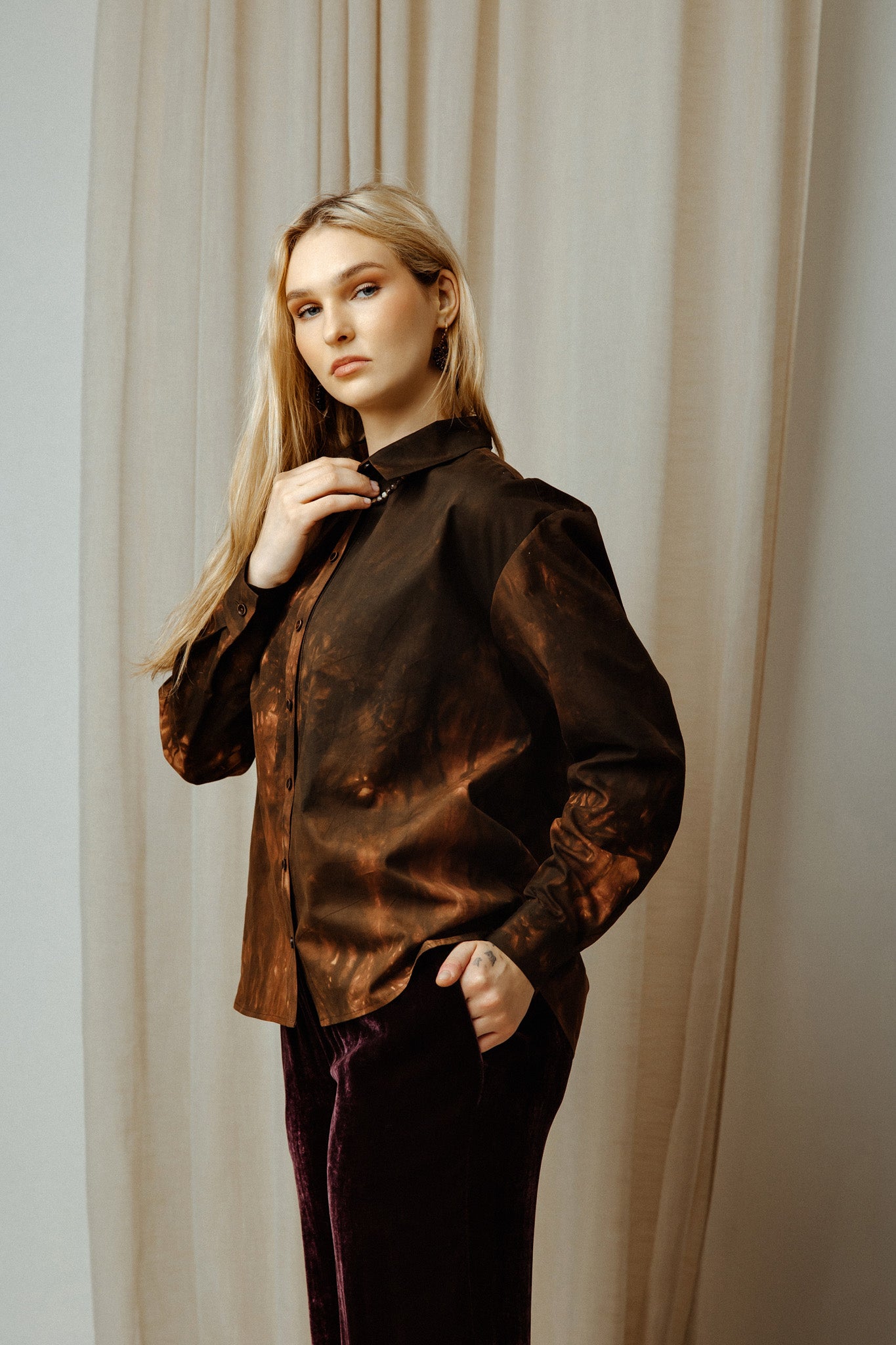 Woman wearing a dark brown colours tye dye boho shirt against a beige curtain background