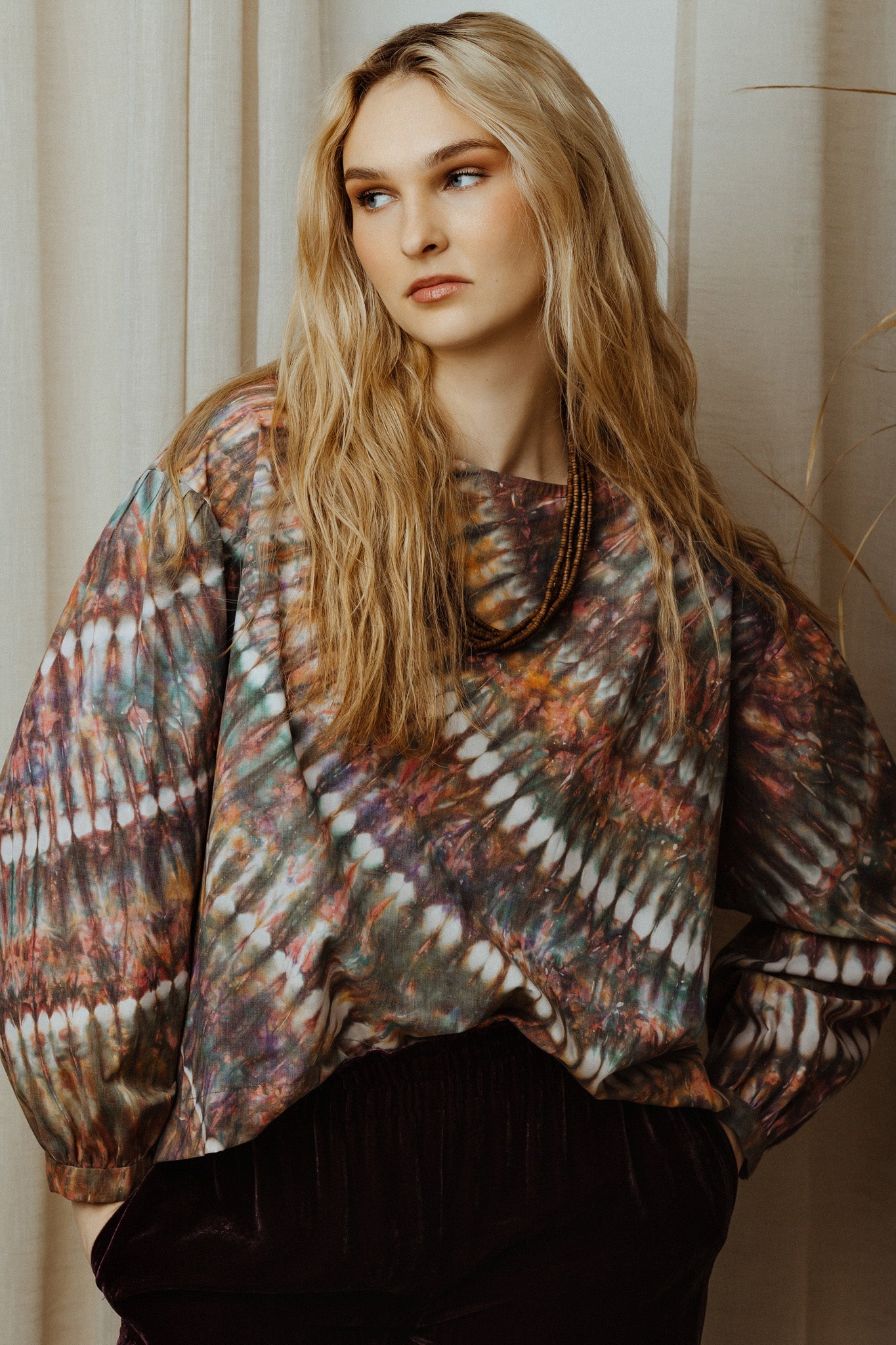 Woman wearing a colourful tye dye blouse against a neutral background