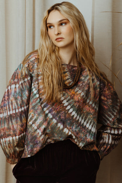 Woman wearing a colourful tye dye blouse against a neutral background