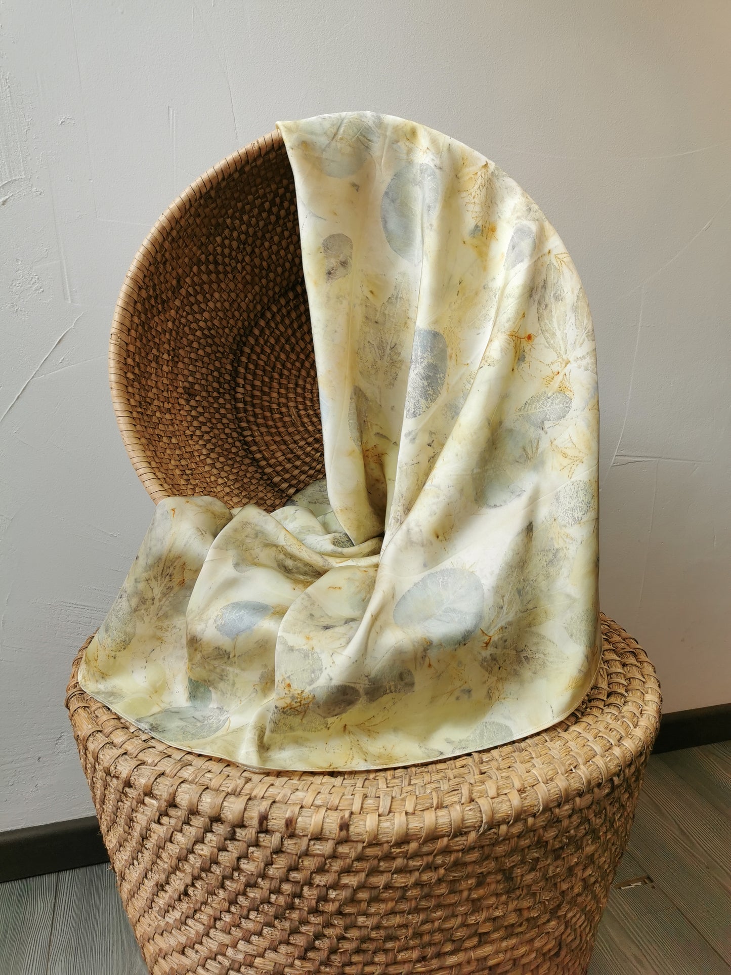 Woven basket with a eco-printed silk scarf draped over it against a plain wall.