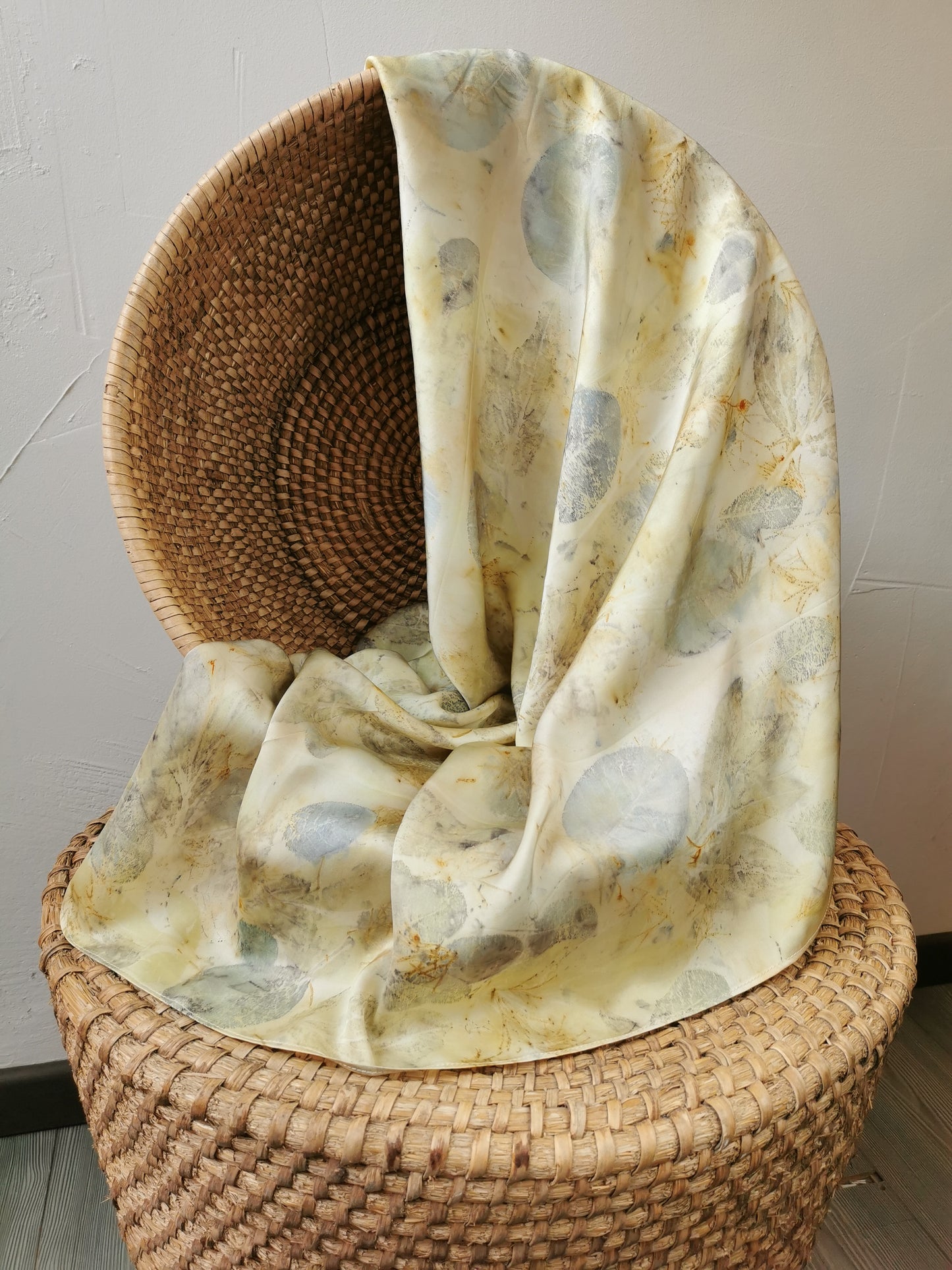 eco-printed citrus silk scarf draped over a woven chair against a neutral background