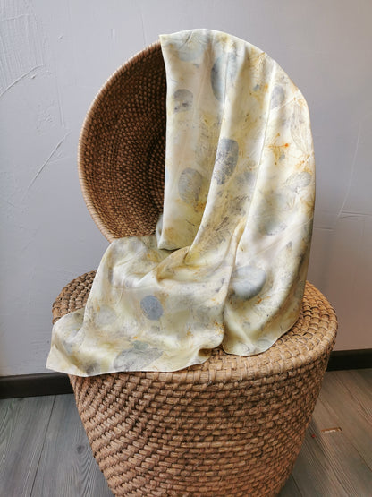 eco-printed citrus silk scarf draped over a woven basket against a plain wall.