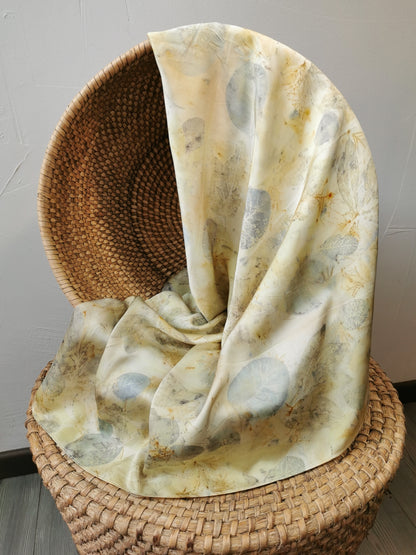 botanically dyed silk scarf draped over a woven basket on a neutral background