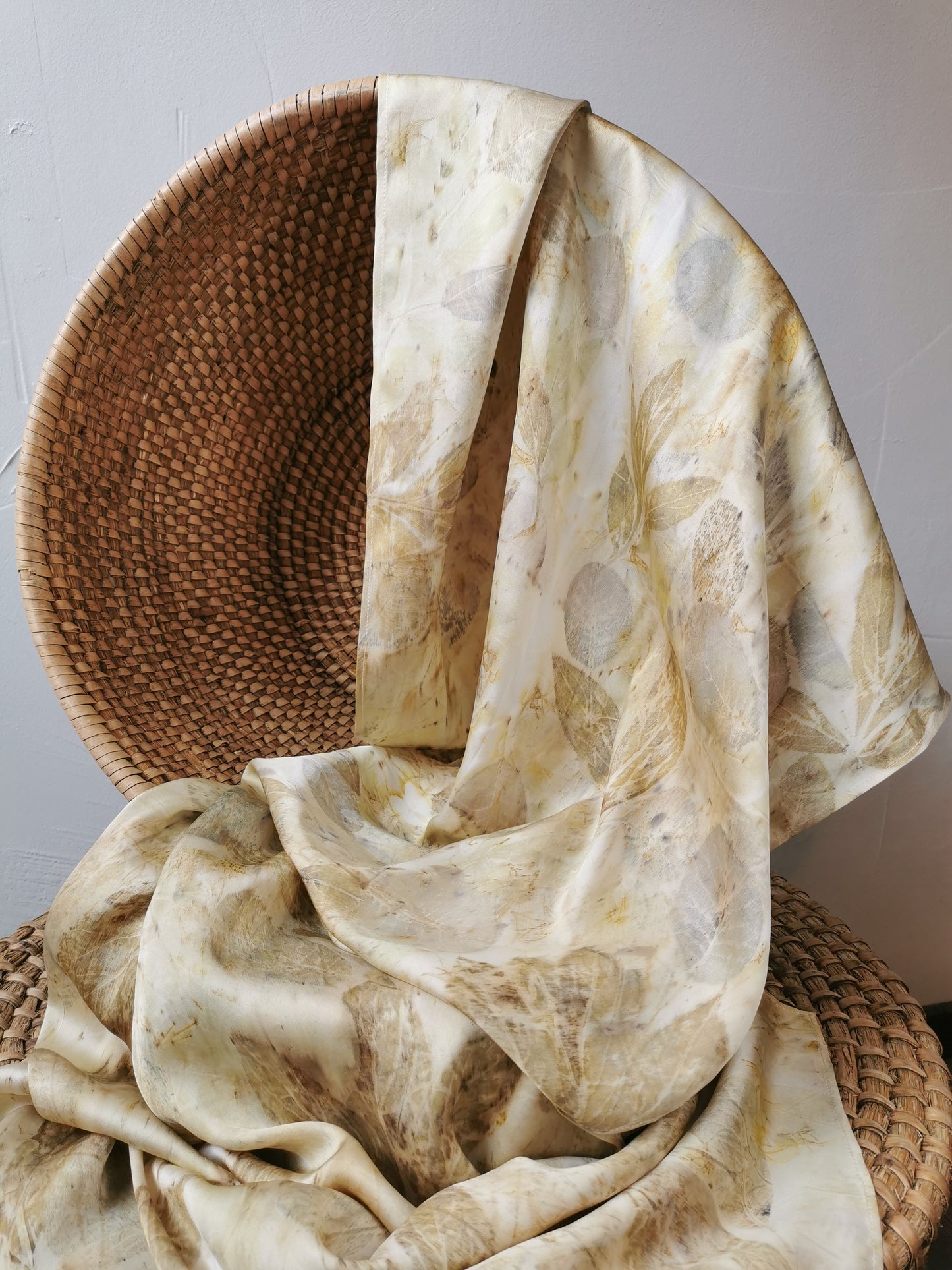 eco-printed silk scarf with floral prints on a woven basket against a neutral background