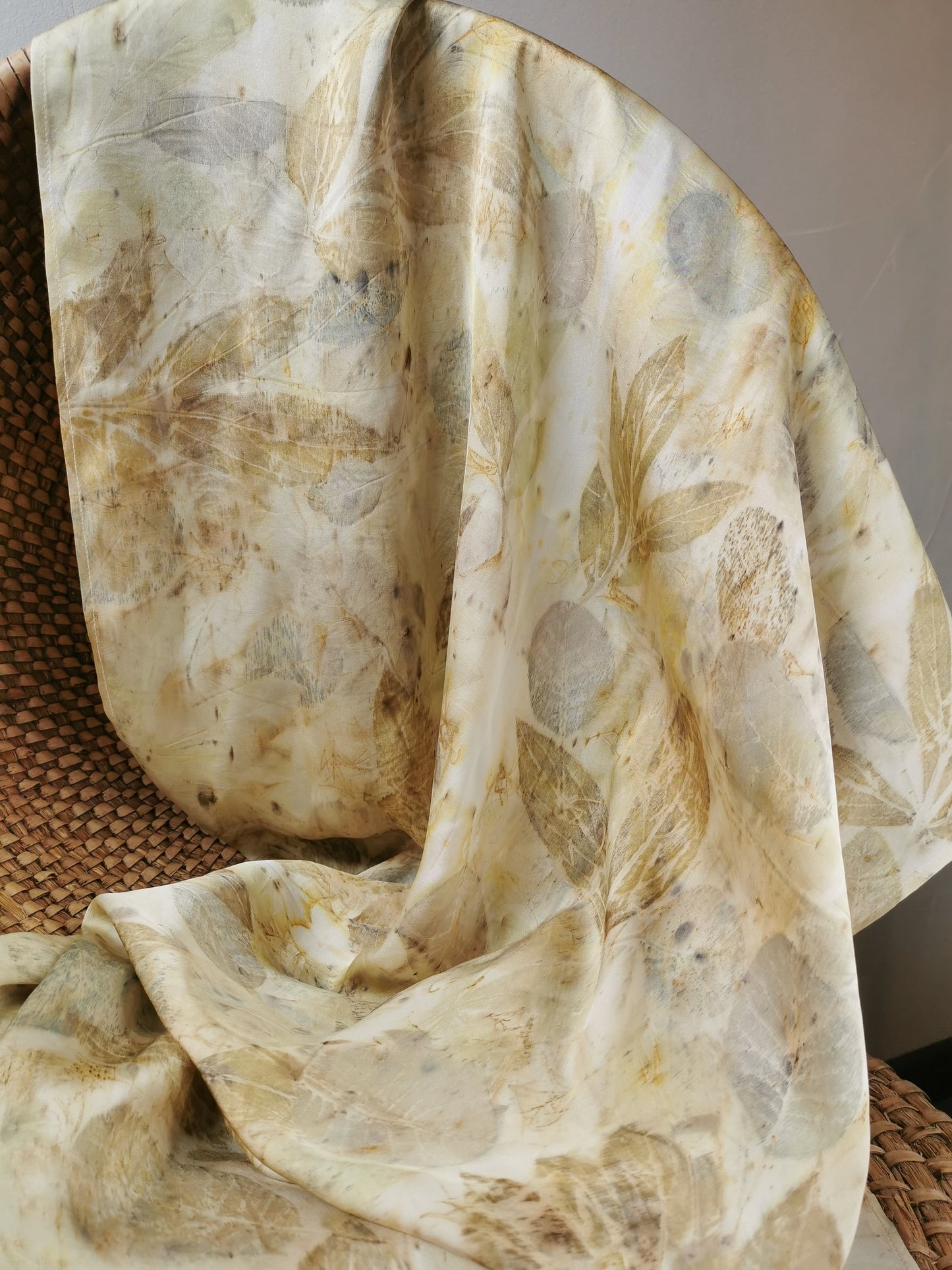 eco-printed silk scarf with floral prints draped over a woven basket on a neutral background