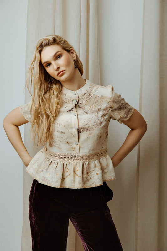 Woman wearing a patterned blouse with ruffled details against a neutral background