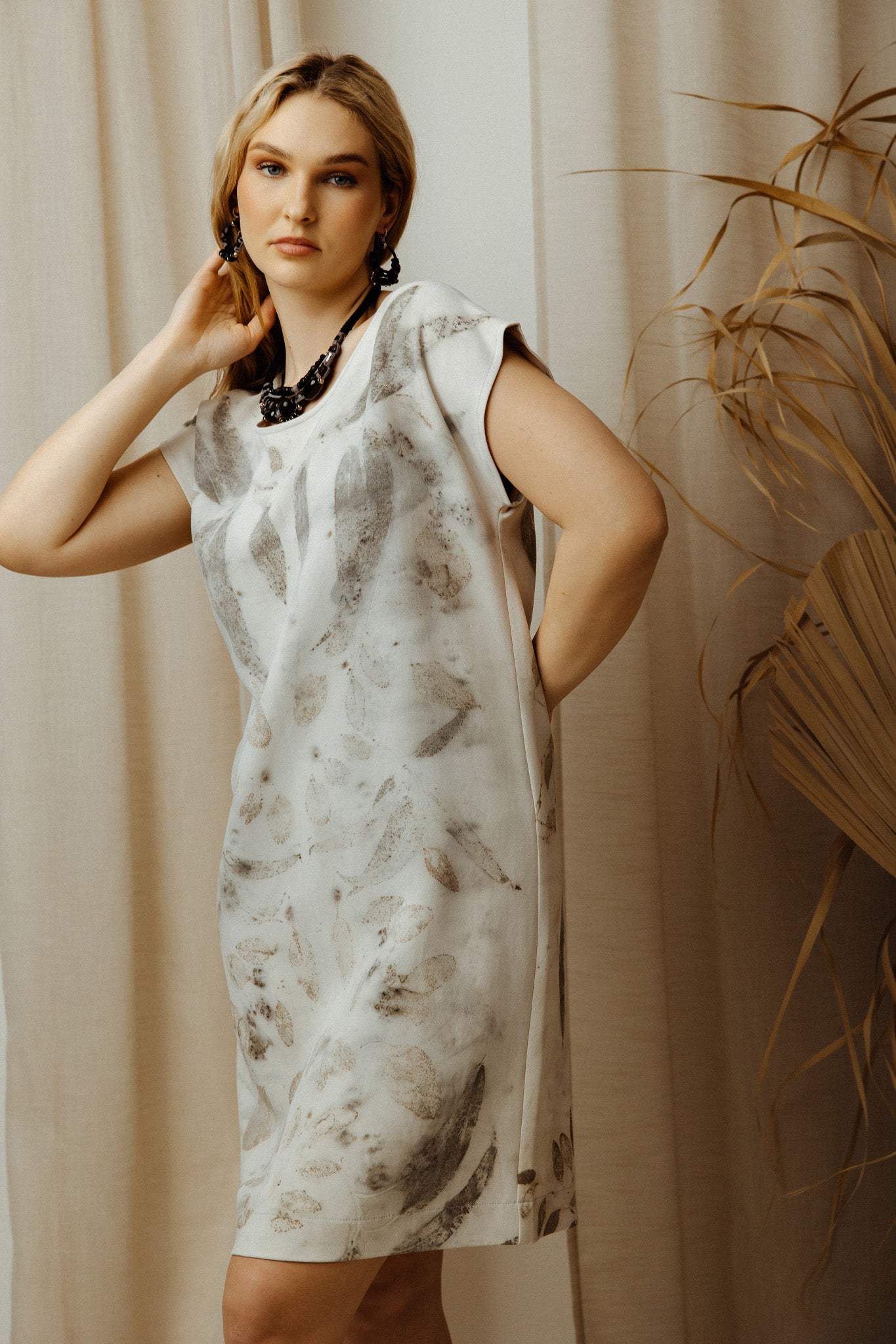 Woman wearing grey eco print viscose dress with a floral pattern against a beige curtain background