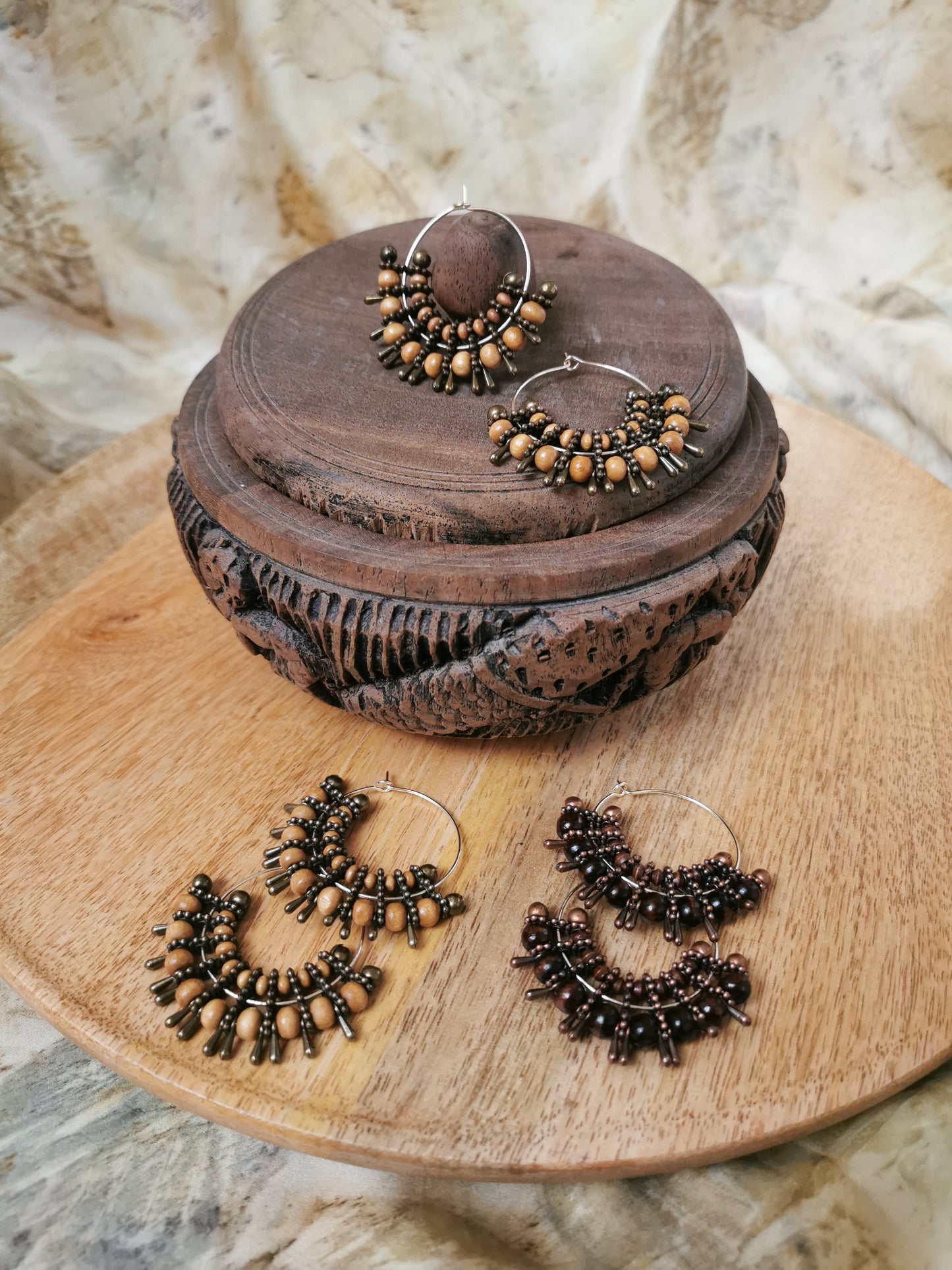 Pair of bronze hoop earrings on a wooden surface with a decorative wooden box.