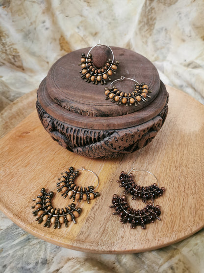 Pair of bronze hoop earrings on a wooden surface with a decorative wooden box.