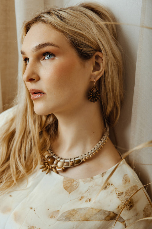 Woman wearing a ivory bead and cord necklace and earrings against a neutral background