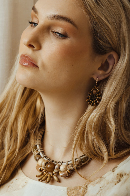 Close-up of a woman wearing ivory bead and cord necklace with a neutral background