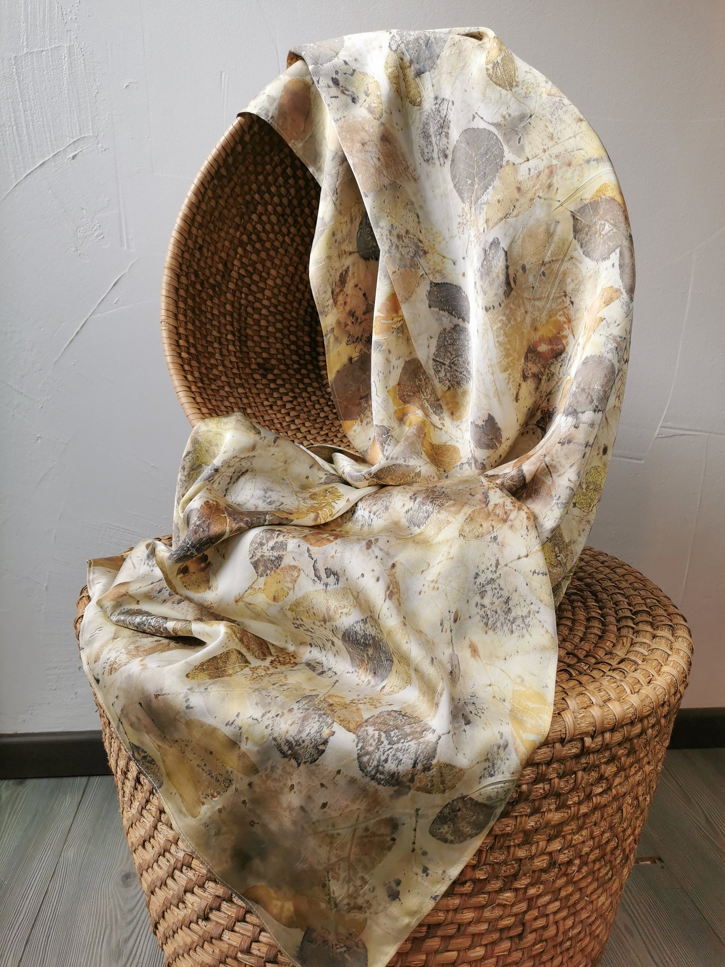 leaf eco-printed silk scarf draped over a woven basket on a light grey background