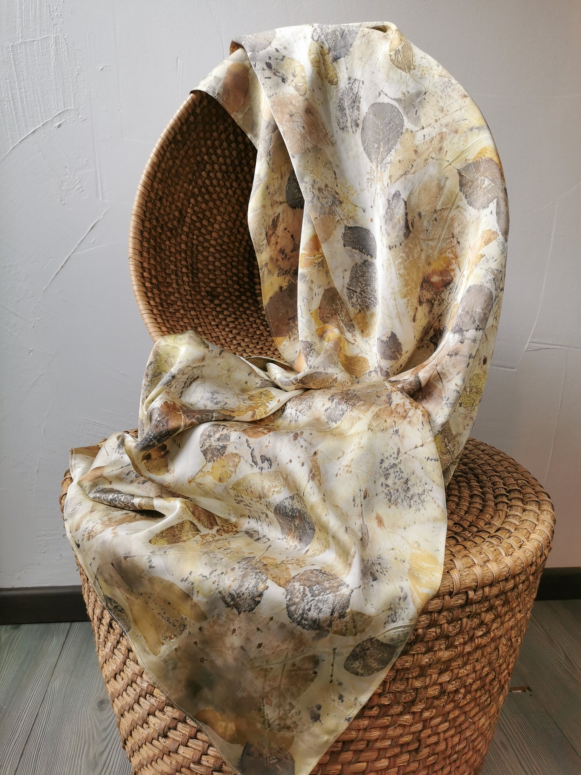 leaf eco-printed silk scarf draped over a woven basket on a light grey background